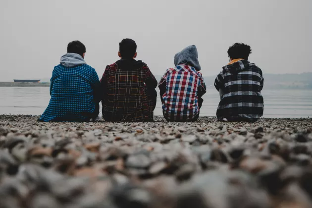 Fyra ungdomar sitter på en strand. Foto: Amir Hosseini, Unsplash.